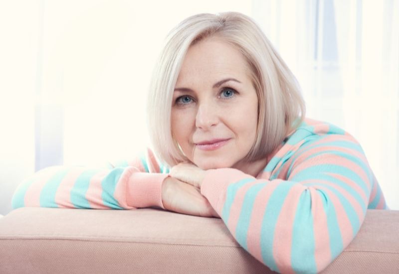 Woman with short blonde hair resting her chin on her arms and smiling, menopause brain fog support