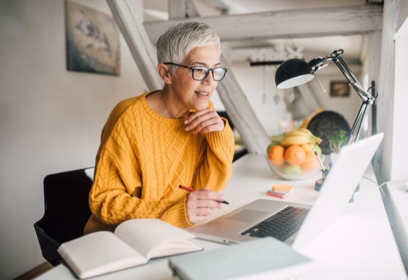 Woman with grey hair smiling while working at a laptop
