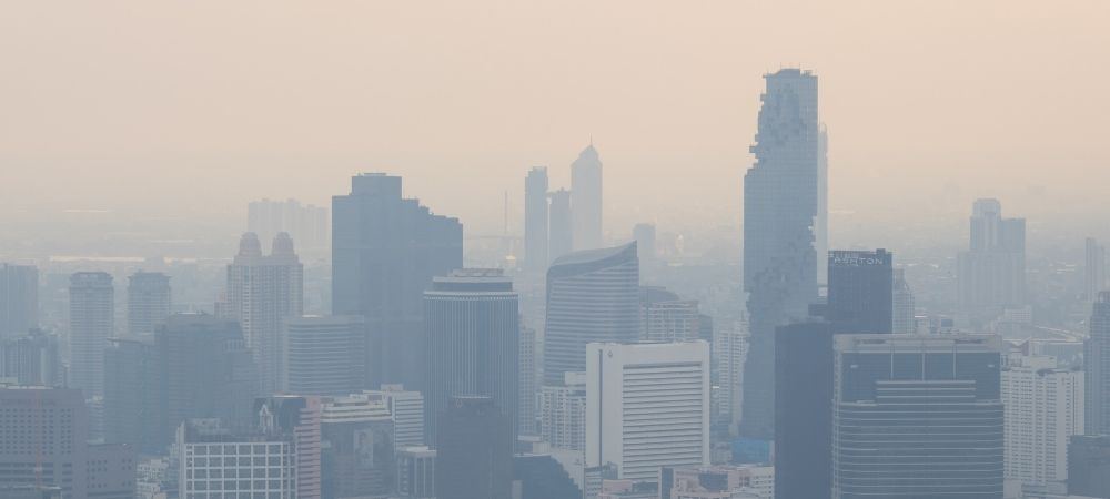 Dense smog shrouds a city skyline, with skyscrapers fading into thick beige haze