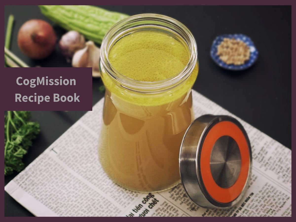 Glass jar of golden bone broth beside its lid, with onion, garlic, bitter melon and parsley; CogMission Recipe Book label