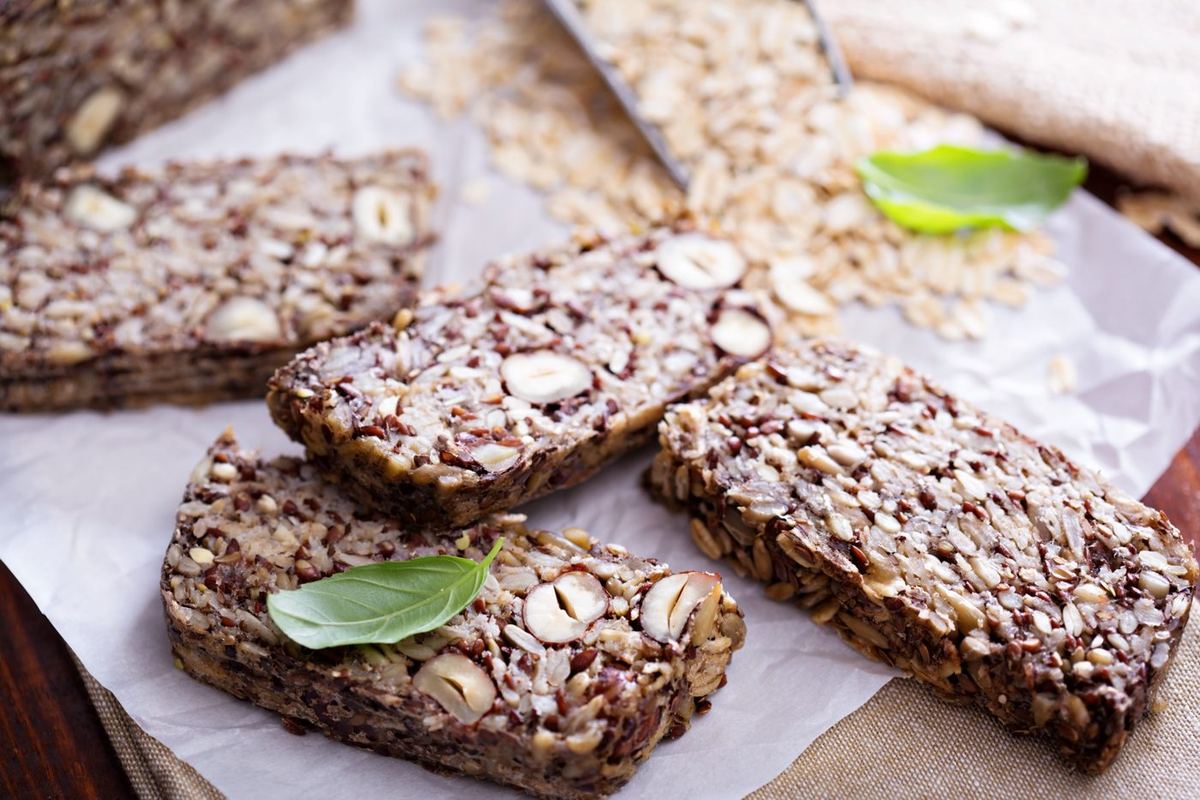 Sliced seeded loaf with whole hazelnuts, flaxseeds and sunflower seeds on baking paper, with oats and basil leaves