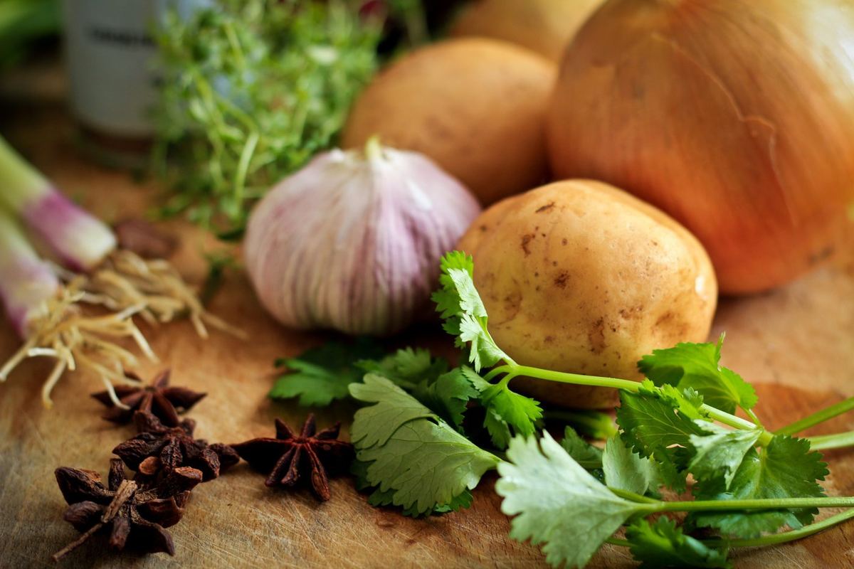 Fresh coriander, garlic, potatoes, an onion, spring onions, thyme and star anise on a wooden chopping board