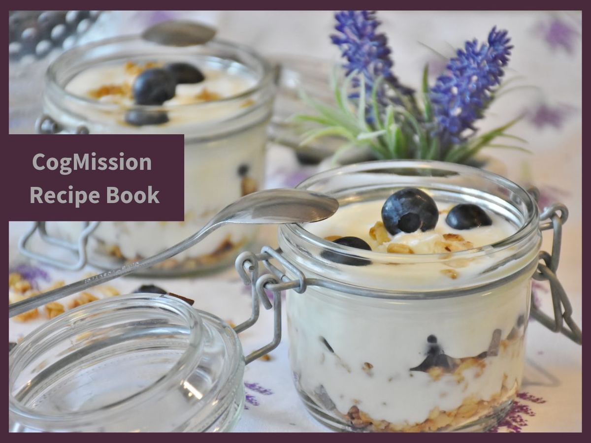 Glass jars of yoghurt layered with granola and blueberries, beside lavender, with a "CogMission Recipe Book" label