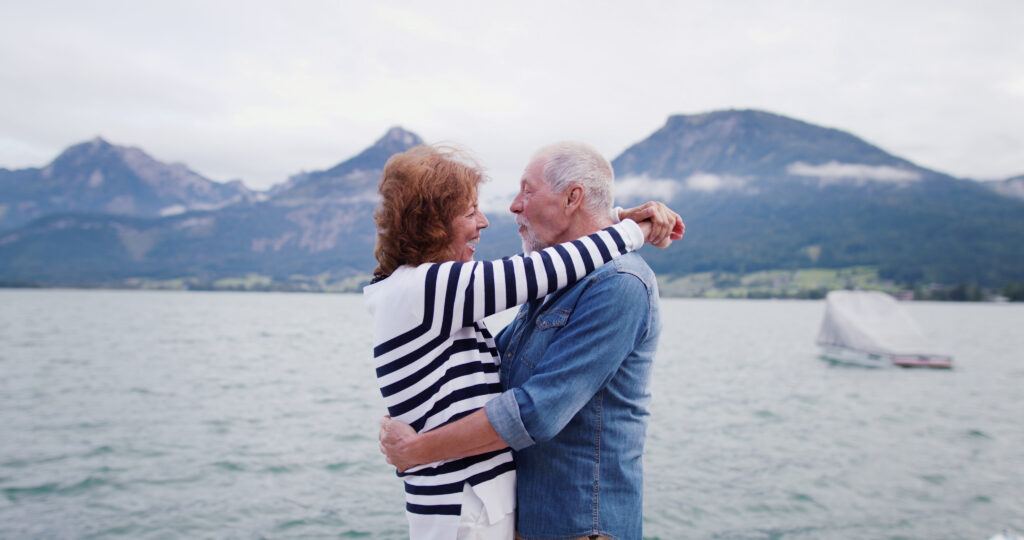 Smiling older couple embracing beside a lake with mountains in the background