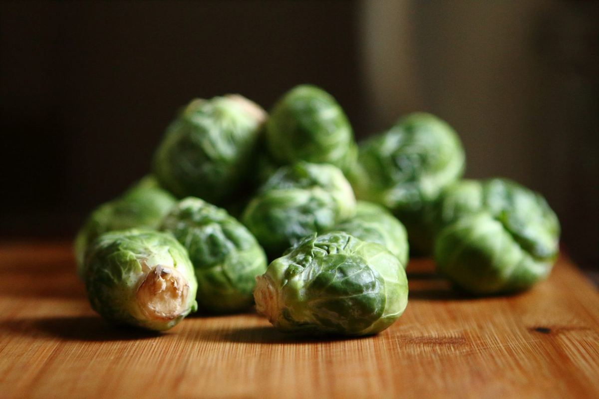 Pile of fresh green Brussels sprouts on a wooden chopping board, lit from the side