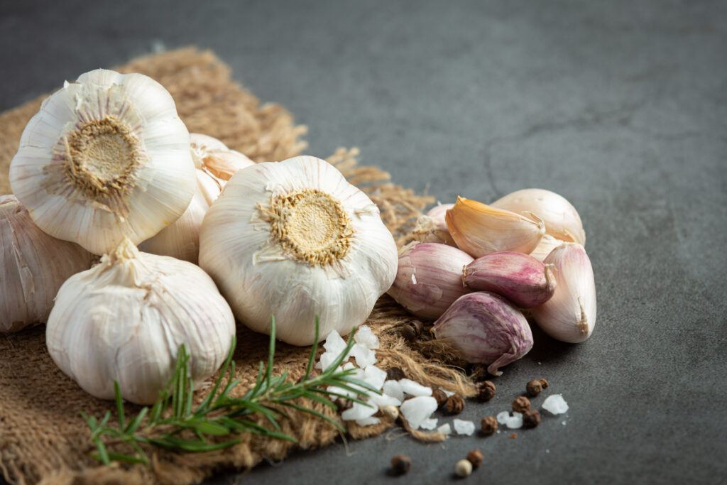 Whole garlic bulbs and pink-skinned cloves on hessian with rosemary, sea salt and peppercorns