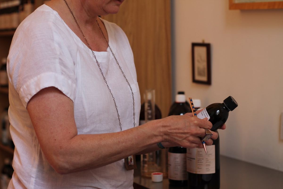 Woman in white linen top examining the label of a dark medicine bottle in a pharmacy or laboratory