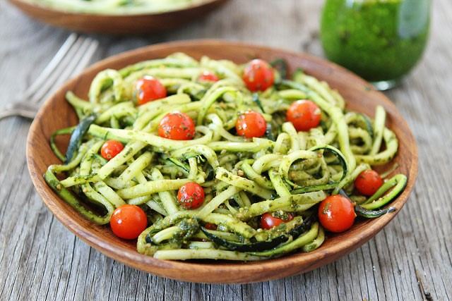 Wooden bowl of courgette noodles tossed in green pesto with cherry tomatoes