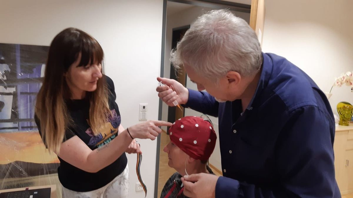Two researchers fit a seated person with a red EEG cap for neurofeedback training