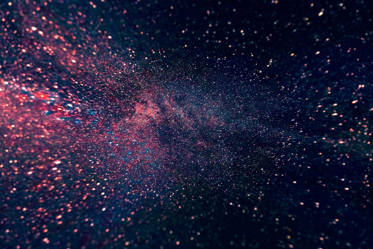 Pink and blue glittering particles scattered across a dark background, resembling a galaxy or starry night sky
