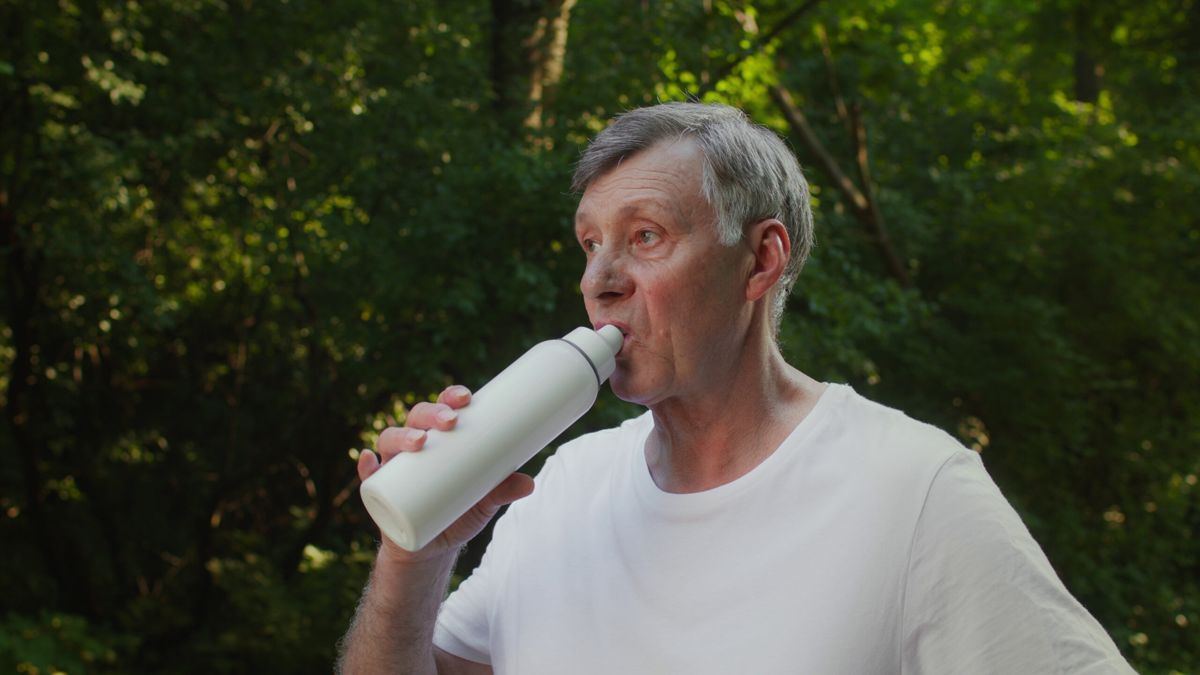 Older man drinking from a water bottle outdoors among trees